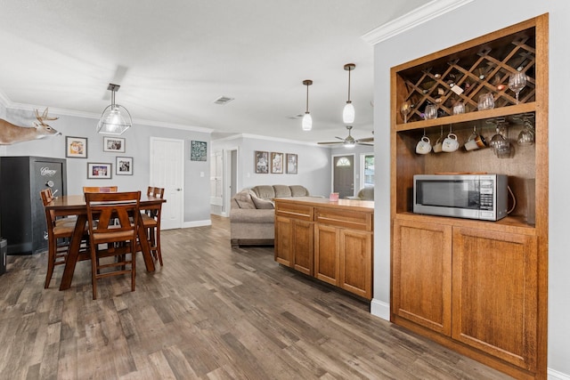 kitchen featuring stainless steel microwave, dark wood-style floors, ceiling fan, brown cabinetry, and ornamental molding