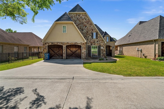 view of front of home featuring fence, driveway, stone siding, a front yard, and an attached garage