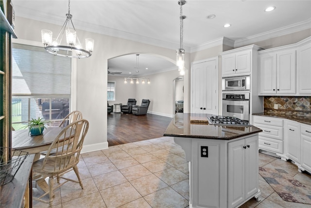 kitchen with stainless steel appliances, a kitchen island, arched walkways, recessed lighting, and a notable chandelier