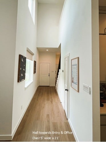 hallway with a towering ceiling, stairway, wood finished floors, and baseboards