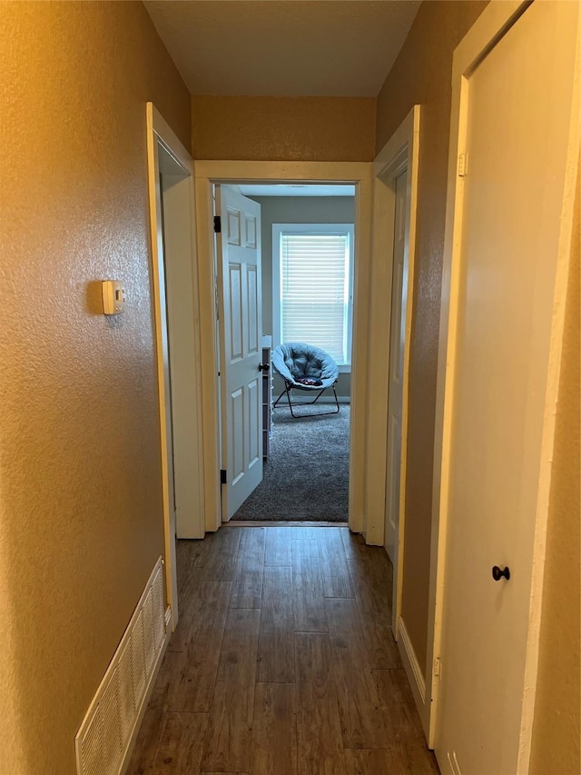 hall featuring baseboards, visible vents, a textured wall, and dark wood-type flooring