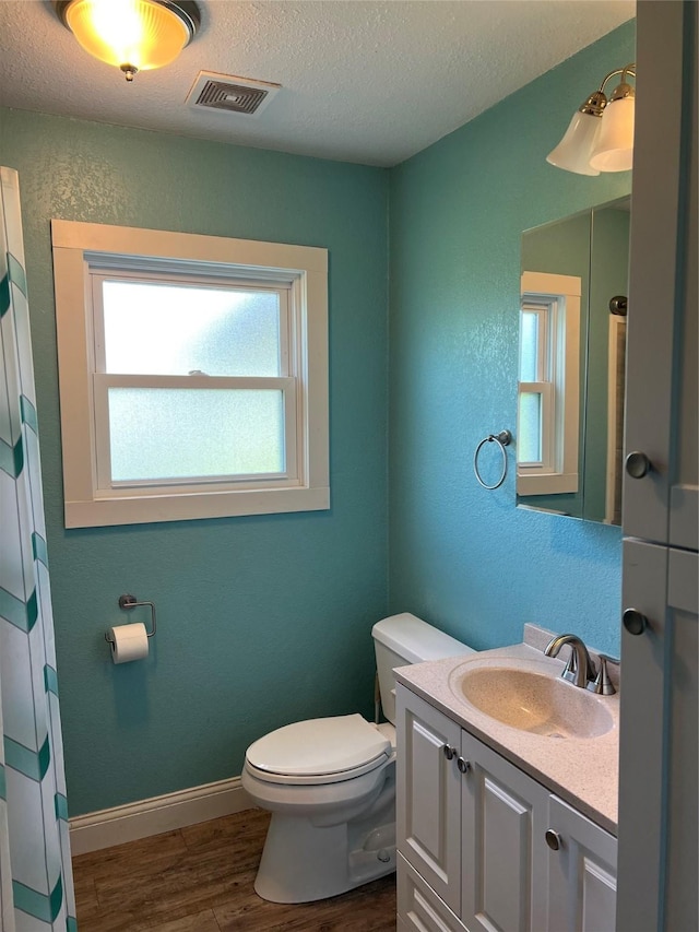 bathroom featuring wood finished floors, toilet, vanity, visible vents, and a textured ceiling