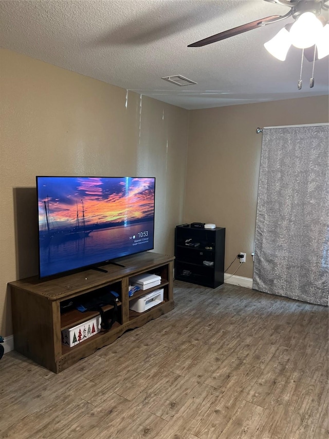 living room with a textured ceiling, wood finished floors, a ceiling fan, and visible vents