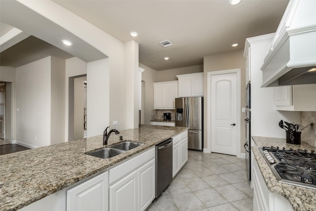kitchen featuring light stone countertops, appliances with stainless steel finishes, a sink, premium range hood, and white cabinetry