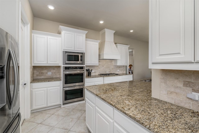 kitchen featuring white cabinets, backsplash, premium range hood, and stainless steel appliances
