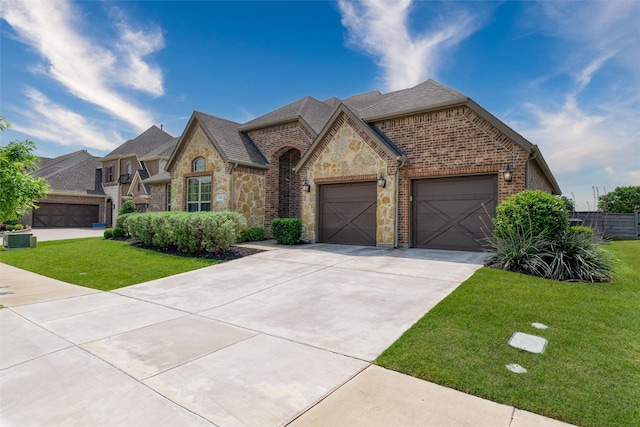 french country inspired facade featuring driveway, a front yard, a garage, brick siding, and stone siding