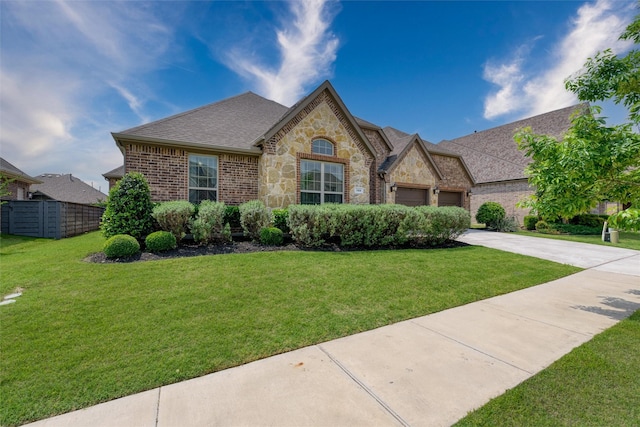 french provincial home with driveway, roof with shingles, a garage, fence, and a front lawn