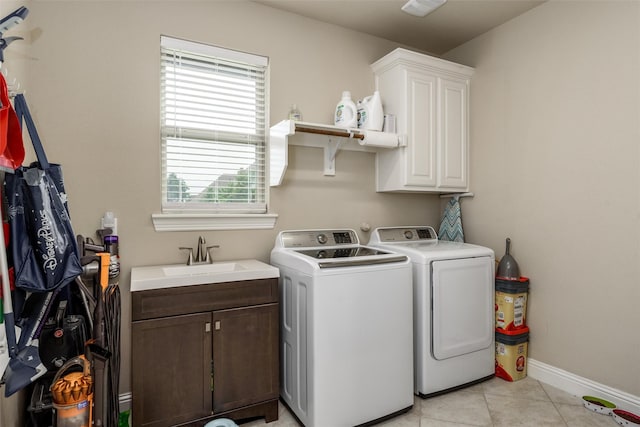clothes washing area with baseboards, washer and clothes dryer, a sink, cabinet space, and light tile patterned floors