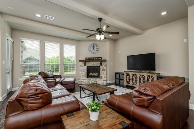 living room with ceiling fan, a stone fireplace, baseboards, beamed ceiling, and visible vents