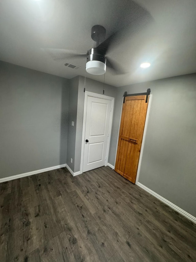 unfurnished bedroom featuring visible vents, a barn door, dark wood finished floors, and baseboards