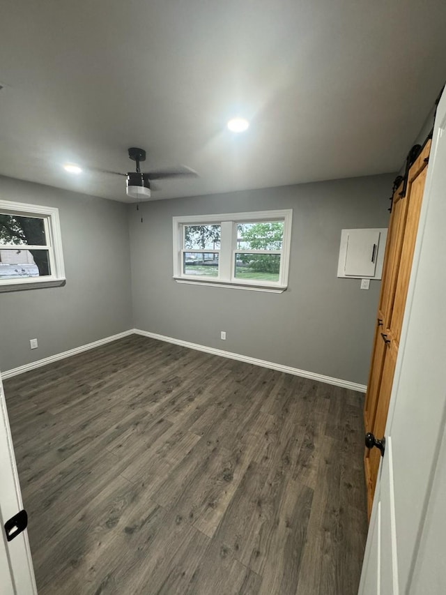spare room featuring ceiling fan, baseboards, a barn door, and dark wood finished floors