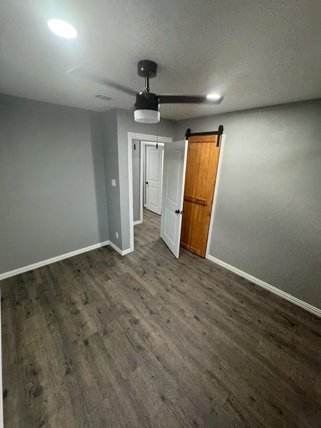 unfurnished bedroom featuring a barn door, dark wood-style flooring, baseboards, visible vents, and a ceiling fan