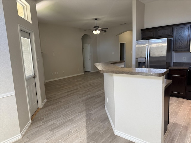 kitchen featuring arched walkways, stainless steel fridge, ceiling fan, baseboards, and light wood-type flooring