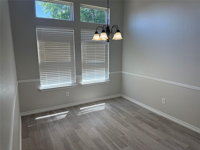 spare room featuring wood finished floors, a notable chandelier, and baseboards