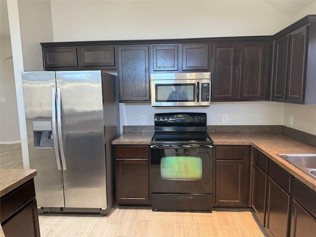 kitchen featuring appliances with stainless steel finishes, dark countertops, light wood-style flooring, and dark brown cabinetry