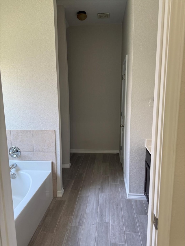 full bath with vanity, visible vents, baseboards, a garden tub, and wood finished floors