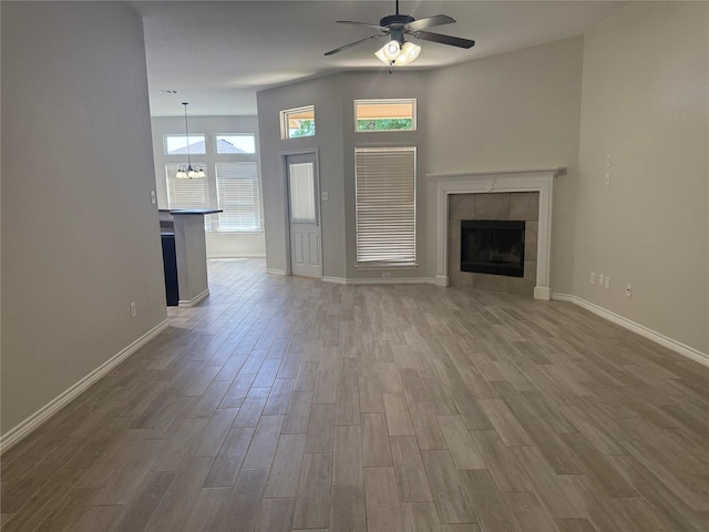 unfurnished living room with a tile fireplace, wood finished floors, baseboards, and ceiling fan with notable chandelier