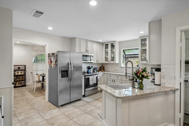 kitchen featuring light stone counters, appliances with stainless steel finishes, backsplash, visible vents, and a peninsula