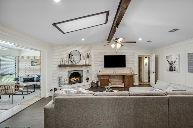 living room with wood finished floors, a brick fireplace, visible vents, a ceiling fan, and lofted ceiling with skylight