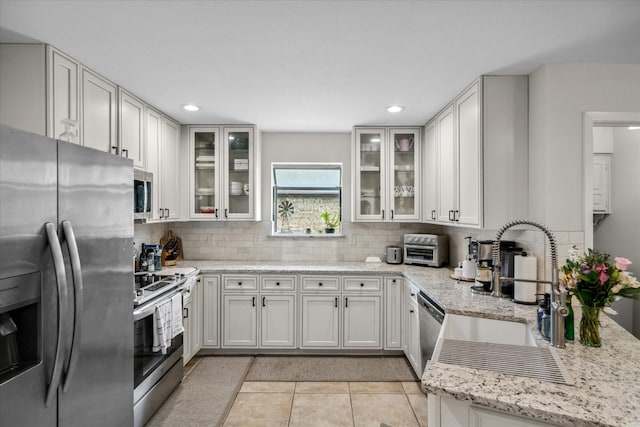 kitchen featuring a sink, light tile patterned floors, tasteful backsplash, light stone counters, and appliances with stainless steel finishes