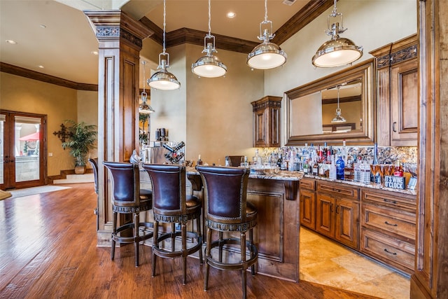 bar featuring crown molding, ornate columns, light wood-type flooring, wet bar, and backsplash