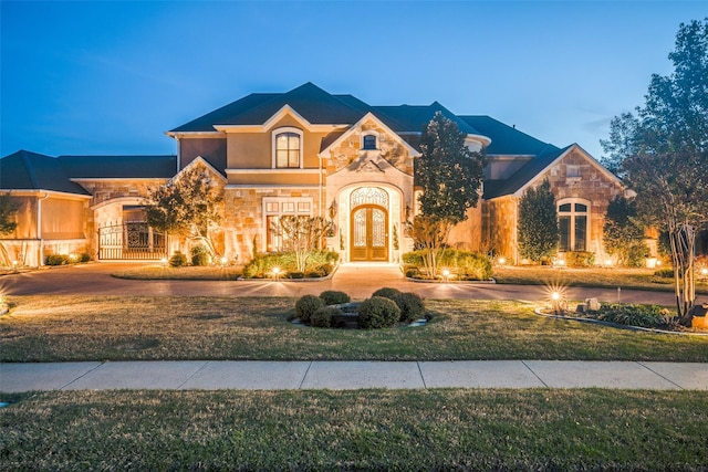view of front of property with stucco siding, french doors, stone siding, and a front lawn