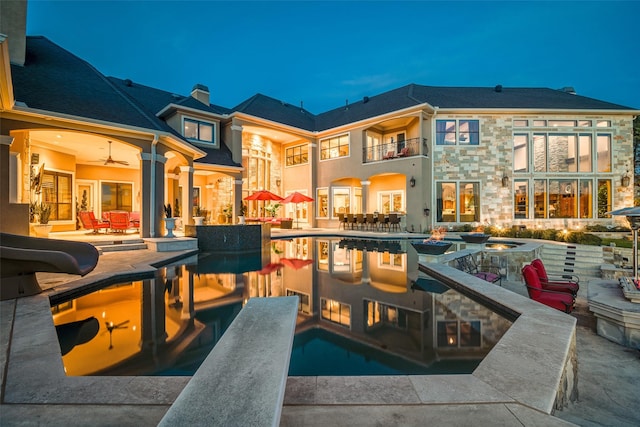 rear view of house with a chimney, an outdoor pool, a patio area, a balcony, and stone siding