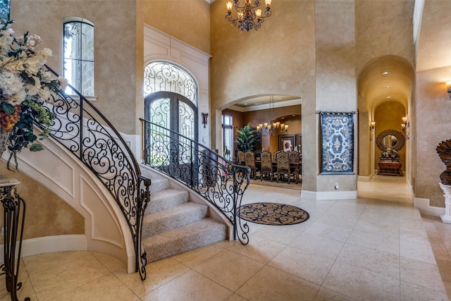 tiled entrance foyer with an inviting chandelier, arched walkways, stairway, and a towering ceiling
