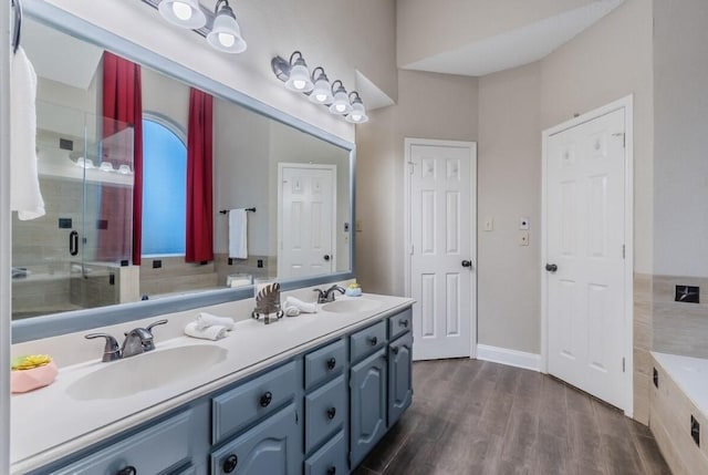 full bathroom with double vanity, wood finished floors, a stall shower, and a sink