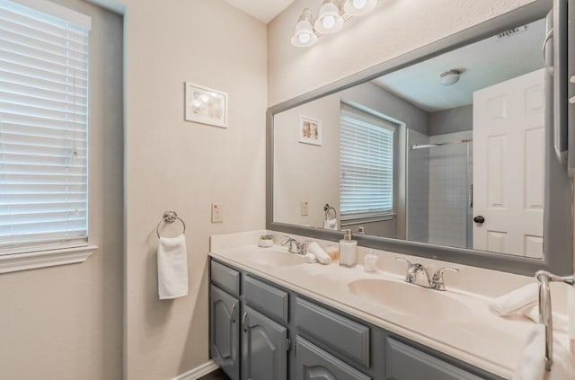 full bath featuring baseboards, walk in shower, double vanity, and a sink