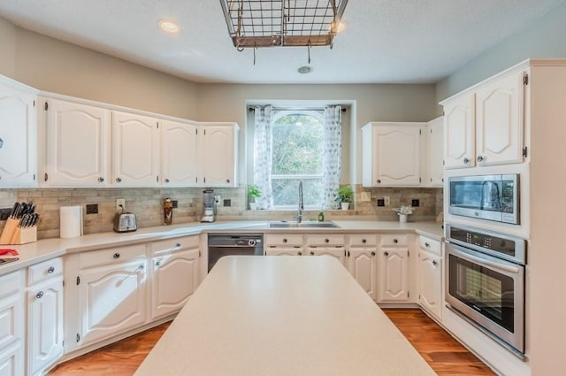 kitchen featuring stainless steel appliances, backsplash, light wood finished floors, and a sink