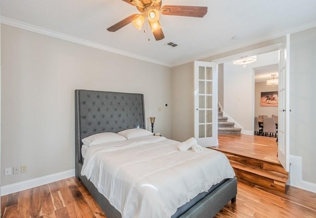 bedroom with wood finished floors, ornamental molding, baseboards, visible vents, and a ceiling fan