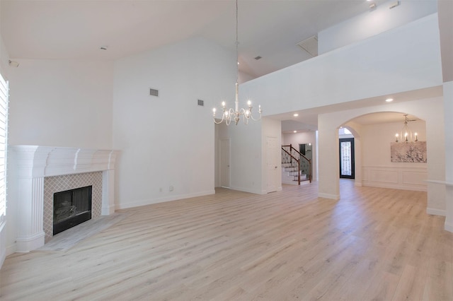 unfurnished living room featuring a chandelier, a fireplace, high vaulted ceiling, light wood-type flooring, and arched walkways