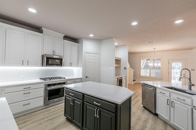 kitchen featuring an inviting chandelier, stainless steel appliances, light wood finished floors, a sink, and white cabinetry