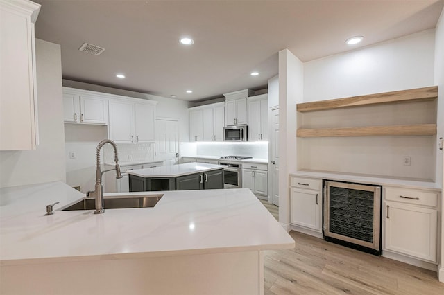 kitchen with beverage cooler, stainless steel appliances, open shelves, a sink, and visible vents