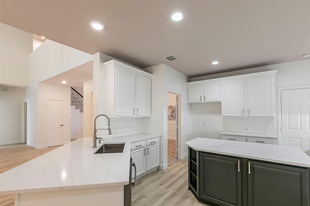 kitchen with white cabinetry, a peninsula, light wood finished floors, and a sink