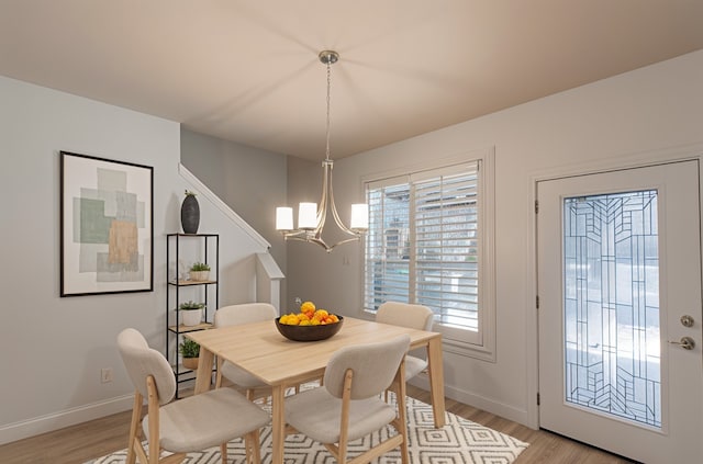 dining space with baseboards, a chandelier, and light wood finished floors