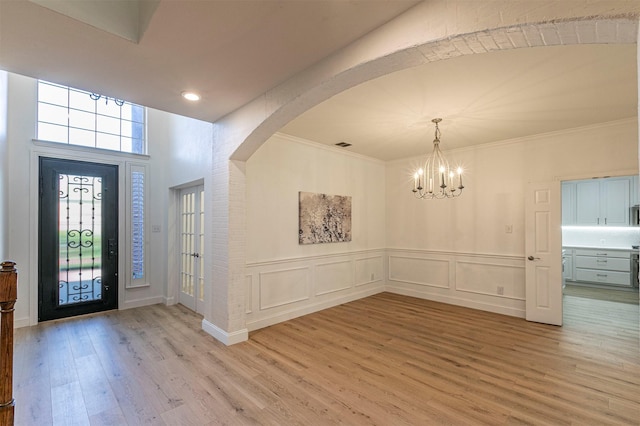 entrance foyer with light wood finished floors, an inviting chandelier, visible vents, ornamental molding, and arched walkways