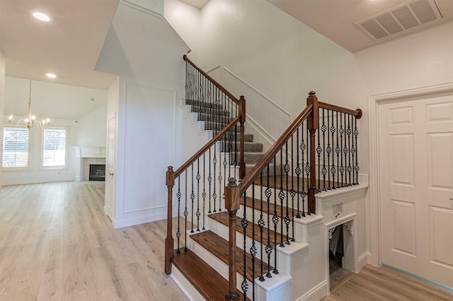 staircase featuring wood finished floors, an inviting chandelier, a premium fireplace, baseboards, and visible vents