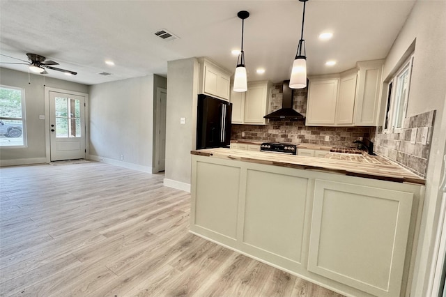 kitchen with visible vents, butcher block countertops, wall chimney range hood, a ceiling fan, and black appliances