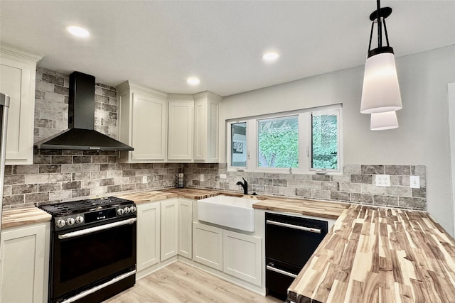 kitchen featuring wall chimney range hood, gas range, a sink, light wood finished floors, and wood counters