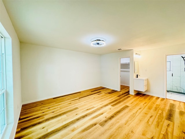 unfurnished bedroom featuring a closet, light wood-type flooring, visible vents, a walk in closet, and baseboards