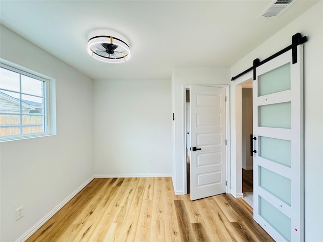unfurnished room with baseboards, visible vents, a barn door, and light wood-style floors