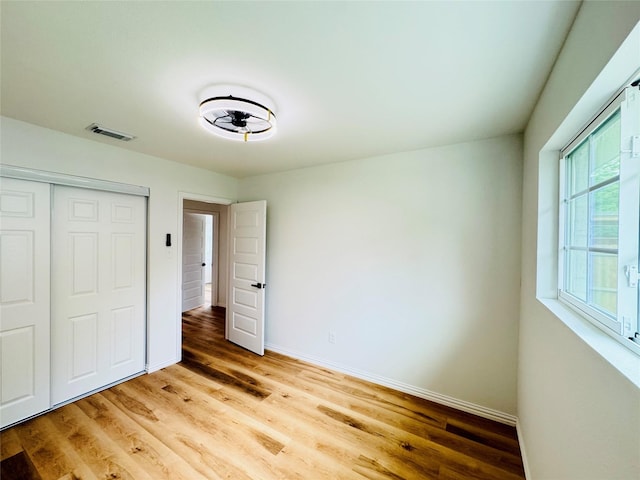 unfurnished bedroom with wood finished floors, visible vents, a closet, and baseboards