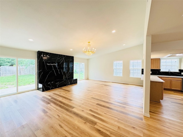 unfurnished living room featuring lofted ceiling, a sink, light wood-style floors, a chandelier, and recessed lighting