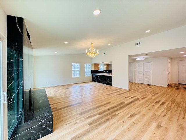 unfurnished living room with visible vents, a chandelier, light wood-style flooring, and vaulted ceiling