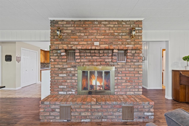 living room featuring a brick fireplace, visible vents, wood finished floors, and baseboards
