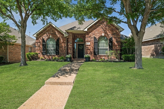 view of front facade featuring a front yard, a shingled roof, and brick siding