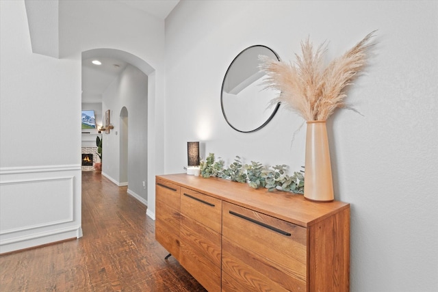 corridor featuring arched walkways, baseboards, and dark wood-type flooring
