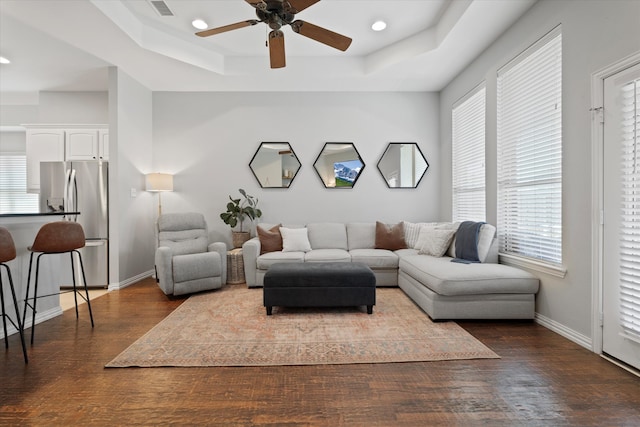 living room with ceiling fan, baseboards, a raised ceiling, and dark wood finished floors